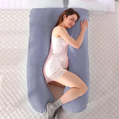 A woman is sleeping on a large U-shaped pregnancy pillow in a bed.
