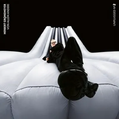A man in black clothing is lying on a white inflatable structure, with a black background behind him.