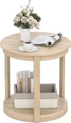 A round, two-tiered side table with a vase of flowers, a cup of coffee, and a magazine on the top surface, and books and a storage basket on the lower shelf.