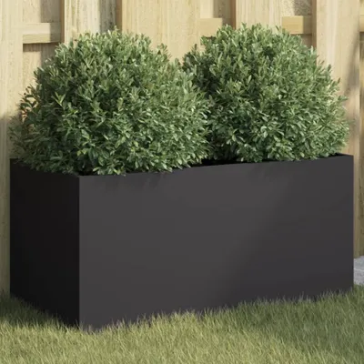 A black rectangular planter filled with two green bushes, placed on grass in front of a wooden fence.