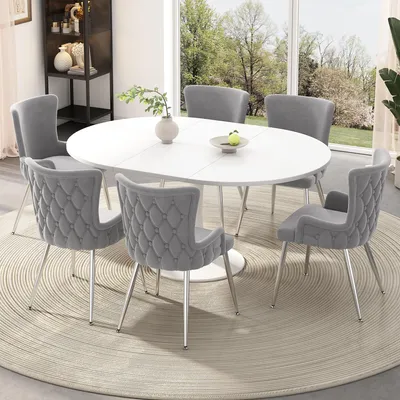 A dining set with a white oval table and six gray chairs, placed on a circular rug in a well-lit room with a large window overlooking a garden.