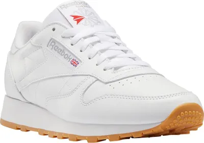 A white Reebok Classic Leather shoe with a gum sole is shown from a side-angle.