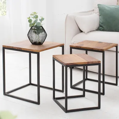 Three nesting side tables with wooden tops and black metal frames are arranged in a living room setting next to a sofa.