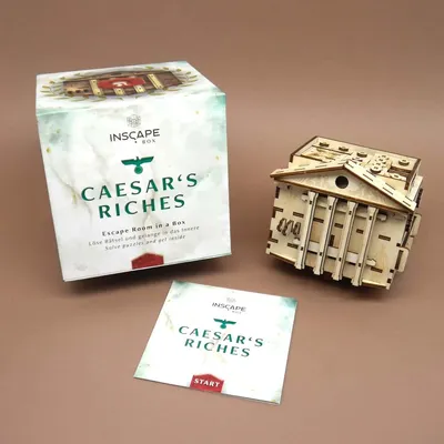 Caesars Riches – Escape Room in a Box mit Holz-Rätselbox, Verpackung und Startkarte auf braunem Hintergrund.