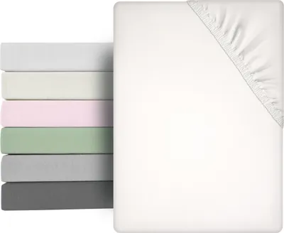 A stack of folded fitted sheets in various colors next to a white fitted sheet.