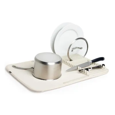 A dish drying mat with a pot, plates, a pot lid, and knives on it, set against a white background.