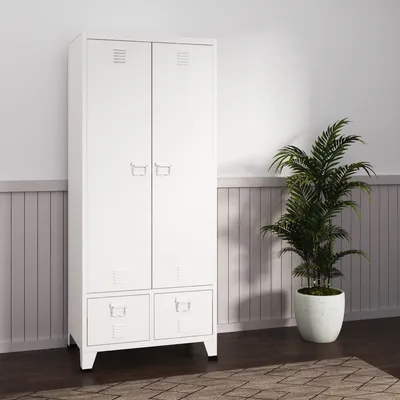 A white wardrobe with two drawers at the bottom stands against a wall with wood paneling. A potted plant is to the right of the wardrobe.