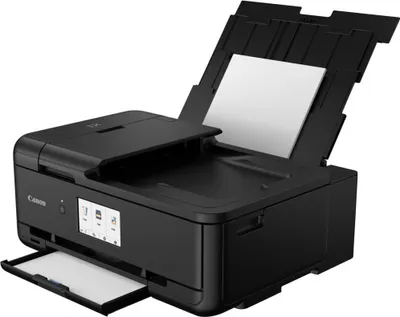 A black Canon PIXMA TS9550 multifunction printer is shown from a diagonal front-left perspective. The scanner lid is open, revealing the scanner bed, and the paper output tray is extended. The automatic document feeder is also open with a sheet of paper in