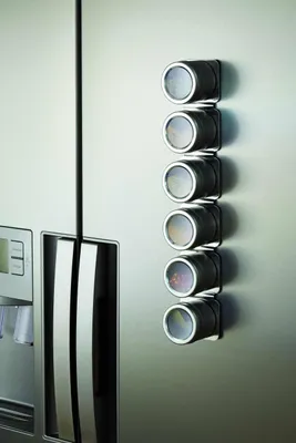 A magnetic spice rack with six spice jars attached to a stainless steel refrigerator door.