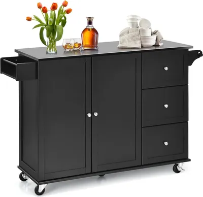 A black kitchen island with a stainless steel top, featuring cabinets, drawers, and wheels, is shown against a white background. Decorative items like flowers, a bottle of alcohol, and dishes are placed on top.