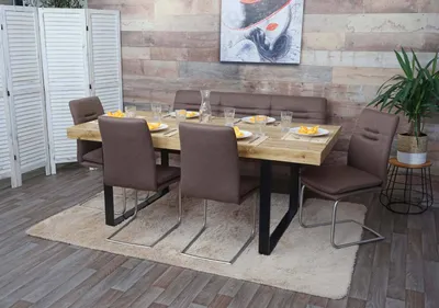A dining room set with a wooden table, brown upholstered chairs and bench, set on a rug in front of a wood-paneled wall with artwork.