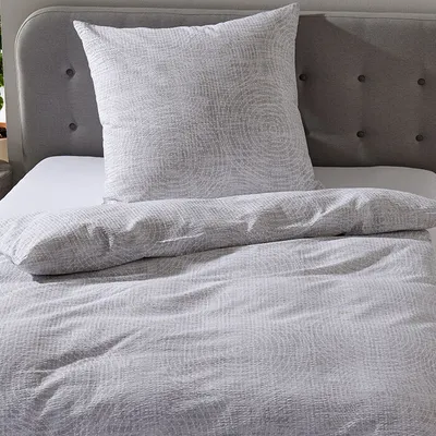 A close-up view of a bed with grey seersucker bedding and a pillow.