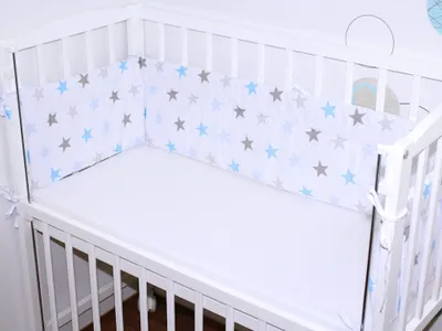 A white baby crib with a white mattress and a white bumper pad with blue and gray stars.