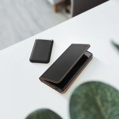 A black leather phone case and a black power bank are placed on a white table.