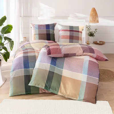 A neatly made bed with a colorful plaid duvet and pillows.