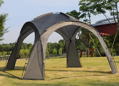 A gray gazebo-like tent is set up on a grassy lawn with trees and a building in the background.