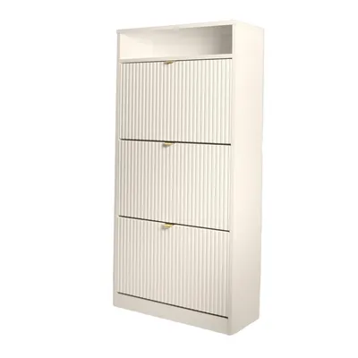 A tall, narrow, white shoe cabinet with three fluted drawers and gold handles is shown against a white background.