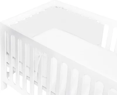 A close-up view of a white crib with a white bumper pad inside.