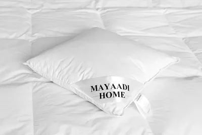 A white pillow with a label on it, placed on a white quilted surface.