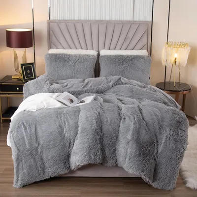 A neatly made bed with plush gray bedding and pillows, set against a backdrop of a modern headboard and bedside tables with lamps.