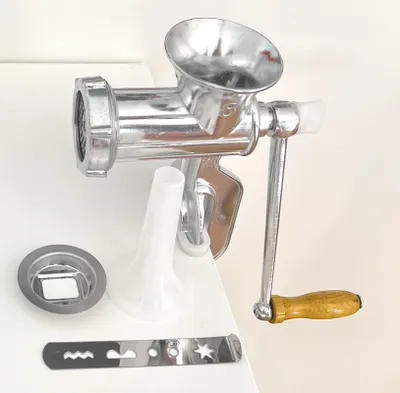 A manual meat grinder and its accessories are displayed on a white surface.