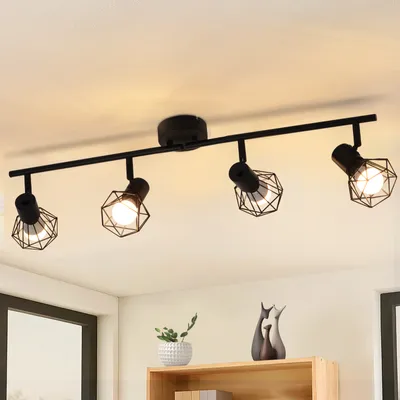 A black ceiling track light with four adjustable spotlights, each with a geometric metal cage shade, is mounted on a white ceiling.