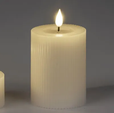 A close-up studio shot of a cream-colored LED candle with a ribbed texture and a flickering flame.