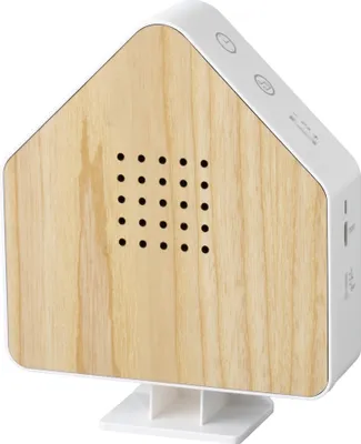 A product shot of a house-shaped sound machine with a wood-grain front panel and white casing, resting on a white stand.