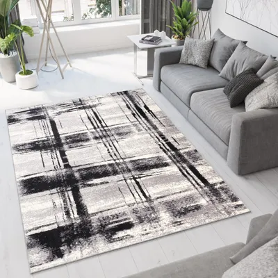A modern living room with a gray sofa and a rug with a black and white abstract pattern.