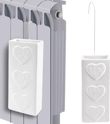 A white ceramic radiator humidifier with embossed hearts is shown hanging on a radiator.