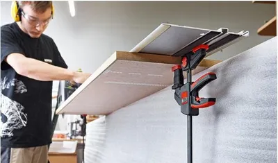 A man is using a clamp to hold a piece of wood while working in a workshop.