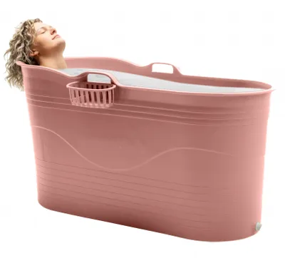 A woman is relaxing in a large pink bath bucket.