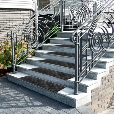Outdoor stairs with decorative metal railings and granite steps. Black rubber mats are placed on the steps for grip.