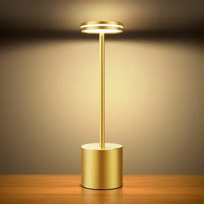 A golden LED table lamp with a circular light at the top, standing on a wooden surface against a gradient brown background.