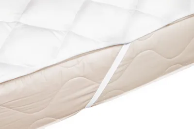 A close-up view of a white quilted mattress topper on a beige mattress, with elastic straps visible.