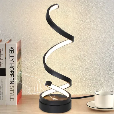 A modern black spiral LED desk lamp is displayed on a wooden surface next to two books and a white coffee cup.