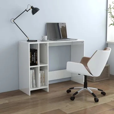 A white computer desk with a bookshelf on the left, a laptop, a cup, and a black desk lamp on top. A white and brown office chair is positioned to the right of the desk.