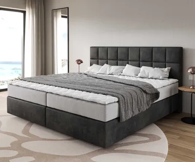 A bed with a headboard and bedding in a room with a large window and a mirror.