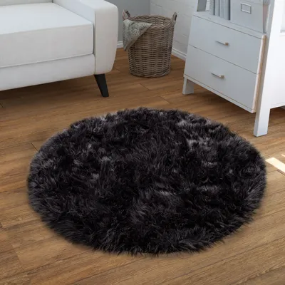 A dark, round, fluffy rug on a wooden floor, next to a white sofa and a wicker basket.
