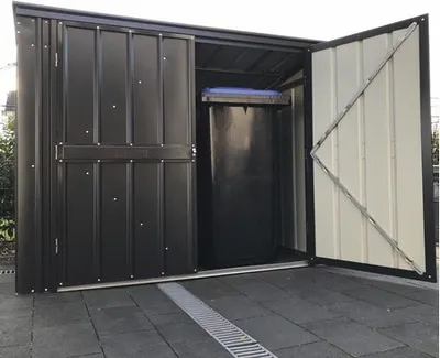 A metal storage shed for trash bins, with one door open and a trash bin inside.