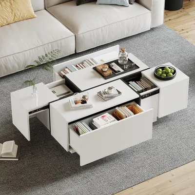 A modern white coffee table with multiple drawers and storage compartments, placed on a grey rug in a living room setting next to a white sofa.