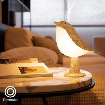 A bird-shaped lamp sits on a marble table next to a book, with a blurred background of a living room.