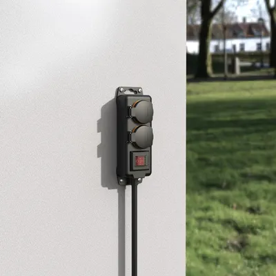 An outdoor power strip mounted on a white wall, with a grassy area and houses in the background.