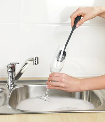 A person is washing a glass in a sink with a brush.