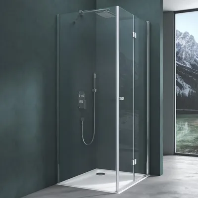 A modern shower cabin with a glass door and silver frame, set against a dark teal wall and a concrete floor. A large window with a mountain landscape is visible in the background.