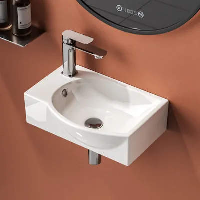 A close-up view of a white ceramic wall-mounted sink with a chrome faucet against a brown wall.