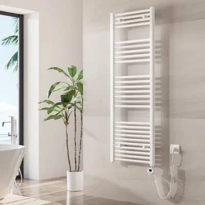 A white electric towel warmer is mounted on a tiled wall in a bathroom, next to a large potted plant and a bathtub.