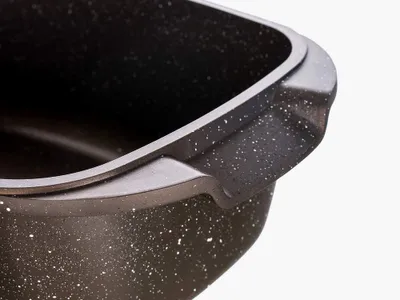 A close-up view of the handle and rim of a dark-colored roasting pan with a speckled pattern.