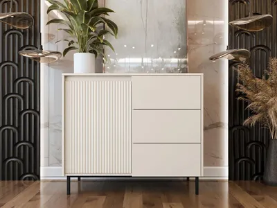 A modern, minimalist kommode with a fluted door and three drawers, placed in a well-lit room with decorative elements.