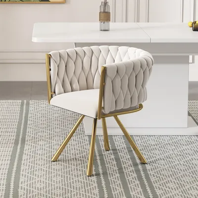 A beige upholstered chair with gold legs sits on a patterned rug in front of a white table.